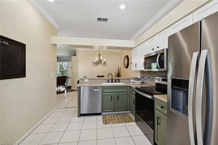 Kitchen featuring a sink, a peninsula, appliances with stainless steel finishes, green cabinets, and a chandelier