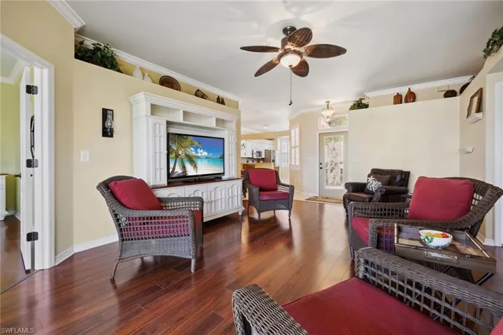 Living room with a ceiling fan, crown molding, wood finished floors, and baseboards