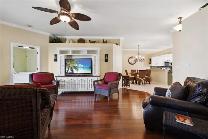 Living area with ceiling fan with notable chandelier, crown molding, and wood finished floors