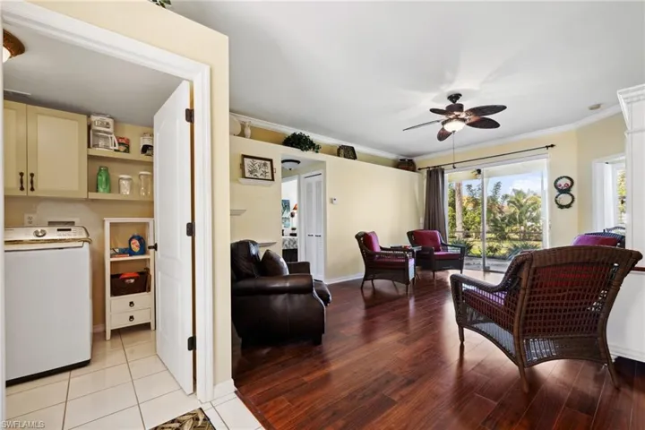 Living room with light wood finished floors, crown molding, baseboards, washer / dryer, and a ceiling fan