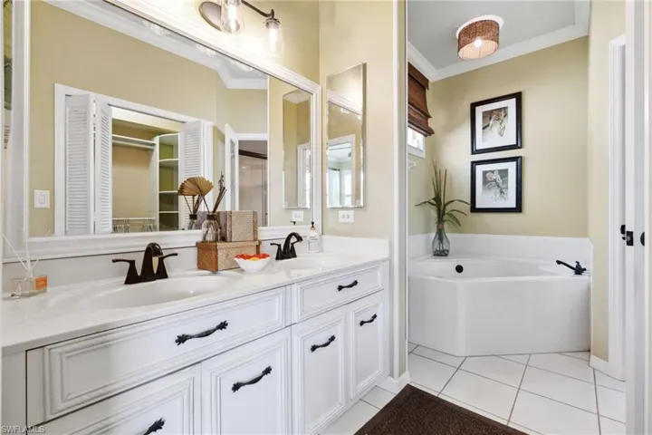 Bathroom with a garden tub, double vanity, a sink, tile patterned flooring, and crown molding