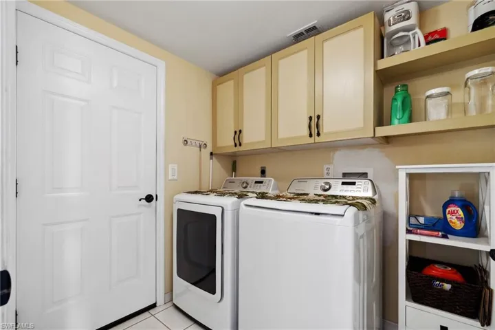 Washroom featuring cabinet space, visible vents, washing machine and dryer, and light tile patterned flooring