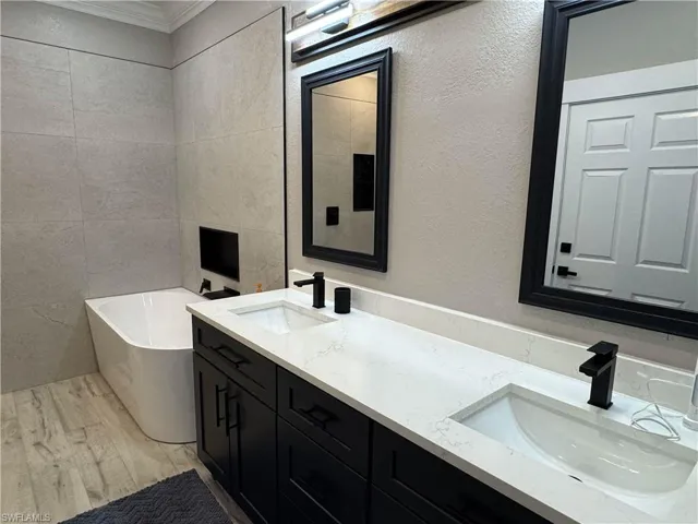 Bathroom with a freestanding tub, tile walls, double vanity, light wood finished floors, and a textured wall