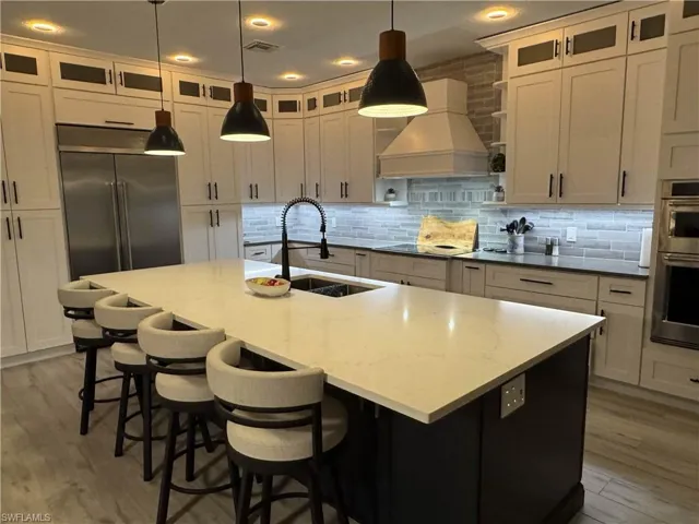 Kitchen with light wood finished floors, glass fronted cabinets, a kitchen breakfast bar, hanging light fixtures, and dual tone cabinetry