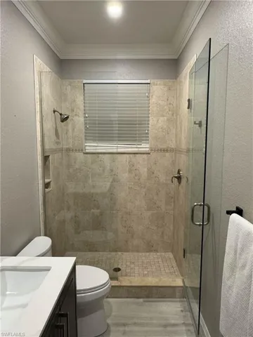 Bathroom featuring a textured wall, vanity, a shower stall, crown molding, and light wood finished floors