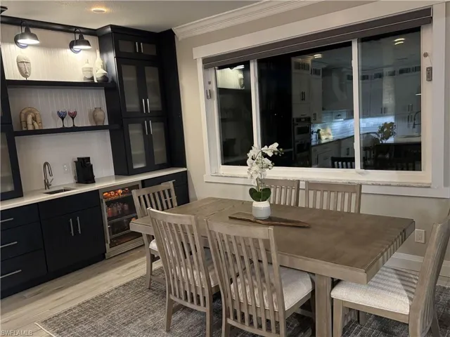 Dining room with light wood-style flooring, ornamental molding, beverage cooler, and bar with sink