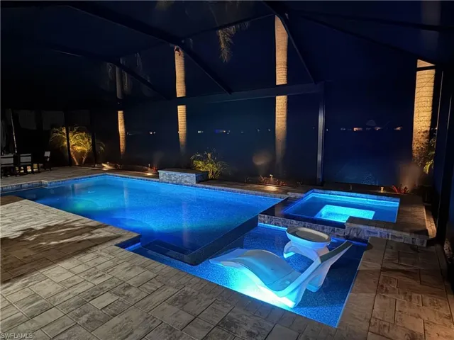 Pool at night featuring a patio area and a pool with connected hot tub