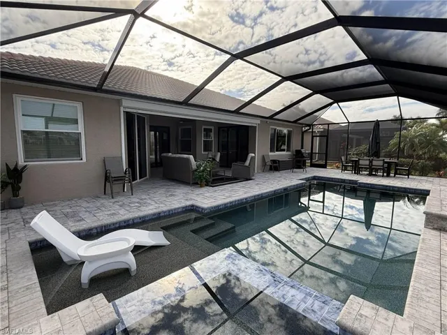 Swimming pool with a sunroom, a patio, glass enclosure, and an outdoor living / dining area