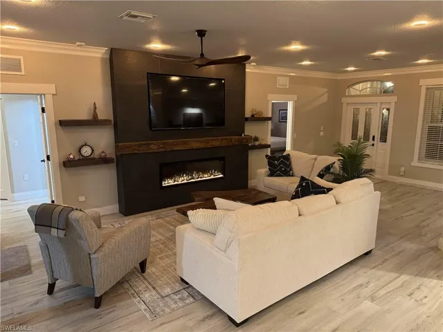 Living room with crown molding, light wood finished floors, a large fireplace, and ceiling fan
