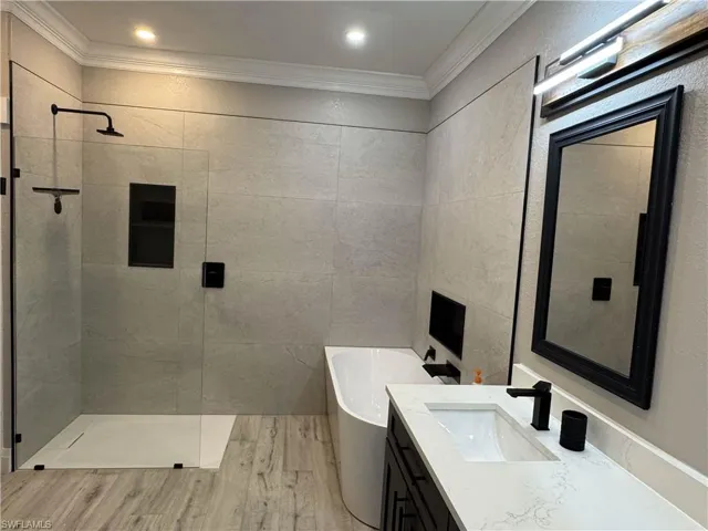 Bathroom with a freestanding tub, vanity, walk in shower, light wood-type flooring, and tile walls
