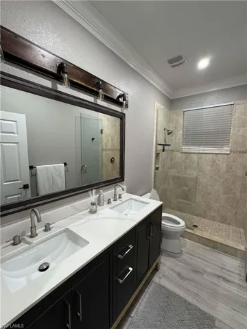 Bathroom with double vanity, ornamental molding, a tile shower, light wood finished floors, and a textured wall