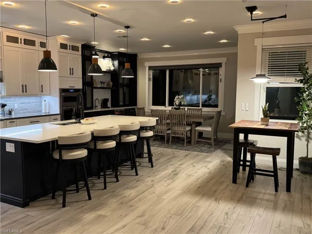 Dual tone kitchen with tasteful backsplash, decorative light fixtures, a kitchen bar, crown molding, and light wood finished floors