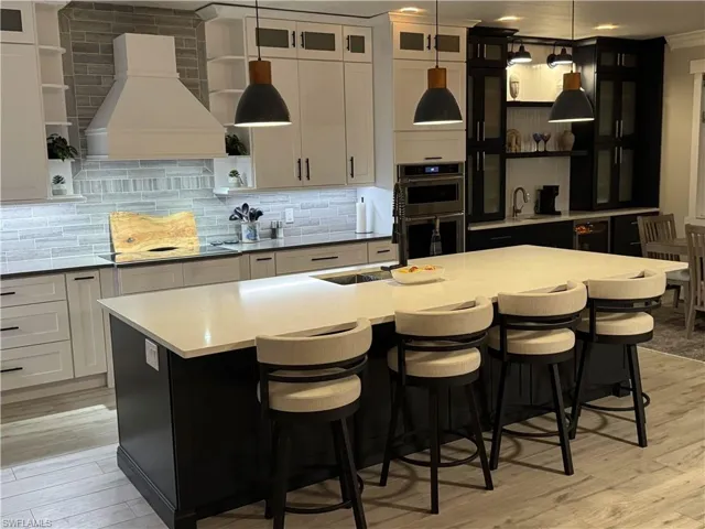 Kitchen featuring open shelves, two tone color scheme, double oven, light wood finished floors, and a center island with sink