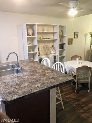 Kitchen with sink, ceiling fan, dark hardwood / wood-style floors, and dark stone counters