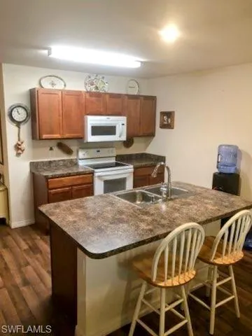 Kitchen featuring a breakfast bar, white appliances, a center island, dark hardwood / wood-style floors, and sink