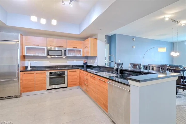 Kitchen with dark stone countertops, appliances with stainless steel finishes, kitchen peninsula, sink, and decorative light fixtures