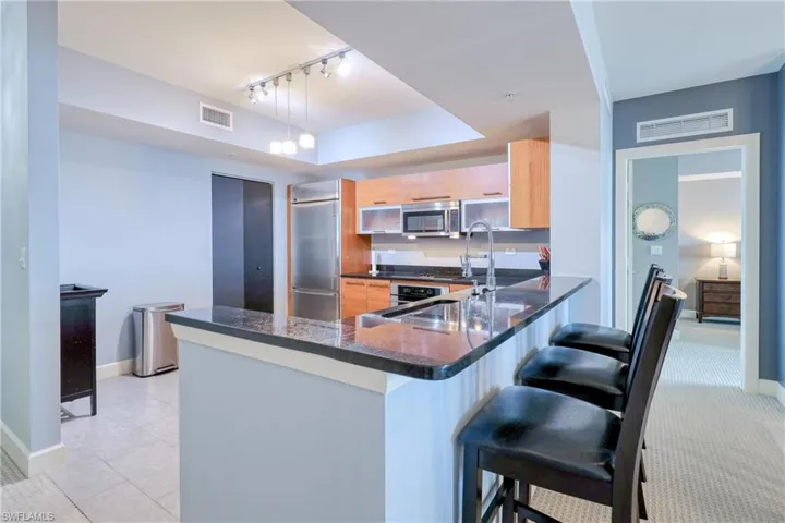 Kitchen with kitchen peninsula, hanging light fixtures, stainless steel appliances, light brown cabinetry, and a breakfast bar
