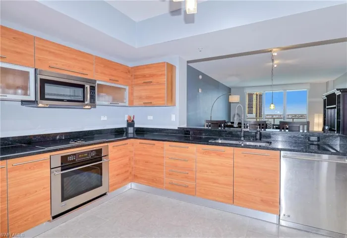 Kitchen with sink, light tile patterned floors, dark stone counters, pendant lighting, and appliances with stainless steel finishes