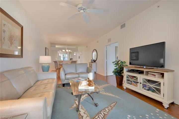 Living room with dark wood-type flooring and ceiling fan with notable chandelier