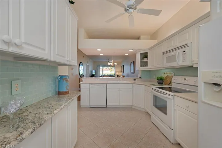 Kitchen featuring white appliances, white cabinetry, kitchen peninsula, and ceiling fan with notable chandelier