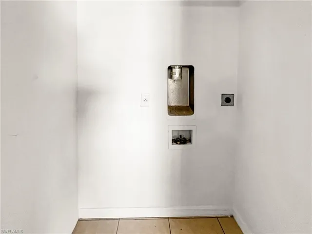 Dedicated utility area with white painted walls, a standard electrical outlet, and connection points for a washing machine and dryer