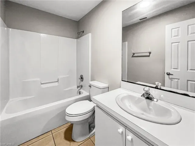 Full bathroom featuring a white tub and shower surround, a white vanity with an integrated sink, a large wall-mounted mirror, a white toilet, and neutral tile flooring