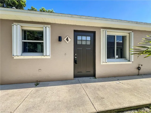 Stucco exterior featuring a dark entry door with decorative glass inserts, two windows with accordion hurricane shutters, and a concrete pathway