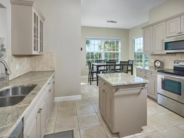 Kitchen featuring decorative backsplash, stainless steel appliances, hanging light fixtures, light stone counters, and light tile patterned floors