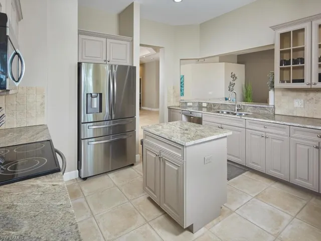 Kitchen featuring backsplash, stainless steel appliances, a center island, light stone countertops, and light tile patterned floors