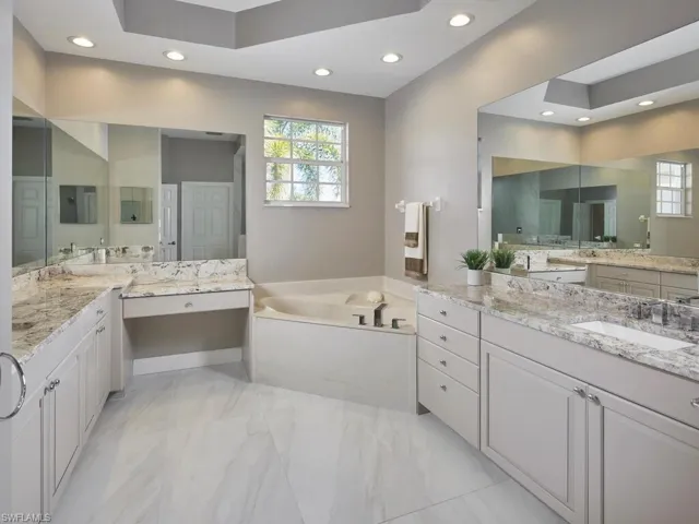 Bathroom with a bath, recessed lighting, two vanities, and light marble finish floors