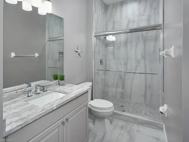 Full bathroom featuring a shower stall, vanity, and marble look tiles