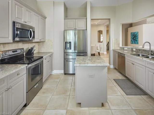Kitchen featuring appliances with stainless steel finishes, tasteful backsplash, a kitchen island, light stone counters, and light tile patterned floors