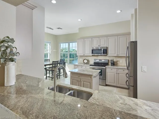 Kitchen featuring appliances with stainless steel finishes, decorative backsplash, light stone countertops, recessed lighting, and a center island