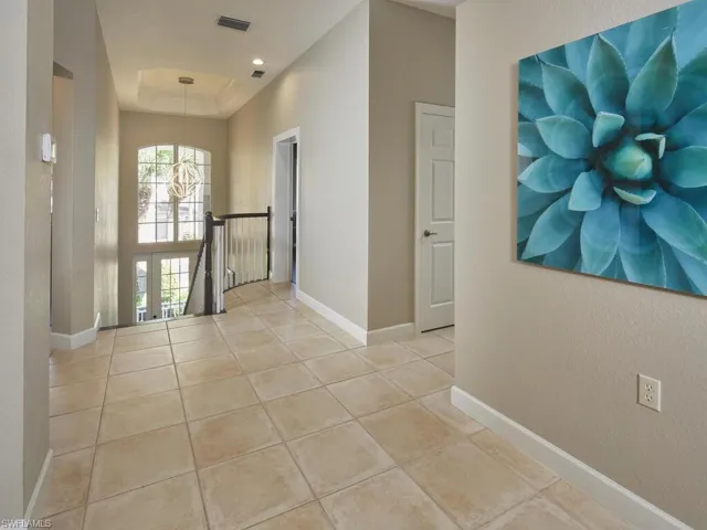 Hall featuring light tile patterned floors, an upstairs landing, a tray ceiling, and a textured wall