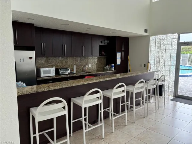 Kitchen featuring dark stone counters, kitchen peninsula, dark brown cabinets, and stainless steel fridge