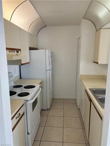 Kitchen with dishwashing machine, sink, range hood, range, and light tile patterned flooring