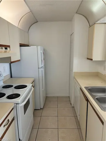 Kitchen with dishwashing machine, sink, exhaust hood, light tile patterned floors, and range