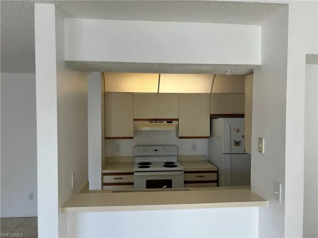 Kitchen featuring kitchen peninsula, light tile patterned floors, white appliances, and a textured ceiling