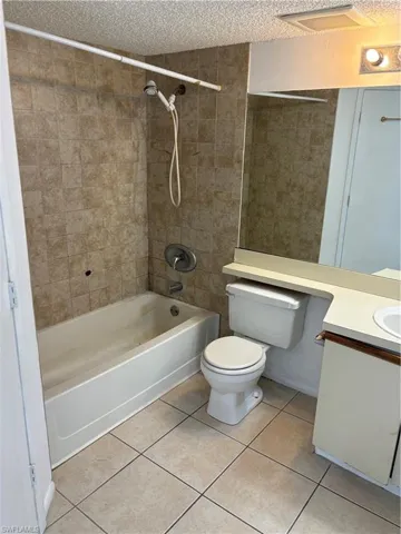 Full bathroom featuring tile patterned floors, tiled shower / bath combo, toilet, and a textured ceiling