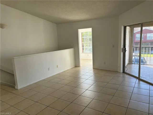 Tiled spare room featuring lofted ceiling, a textured ceiling, and a wealth of natural light