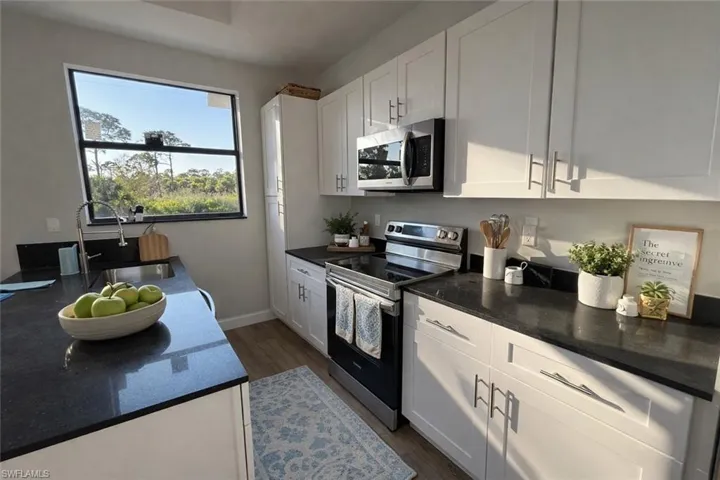 Kitchen with stainless steel appliances, white cabinetry, dark stone countertops, and dark wood-style floors