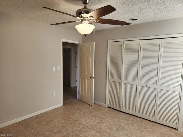 Unfurnished bedroom featuring a textured ceiling, a ceiling fan, a closet, and light tile patterned floors