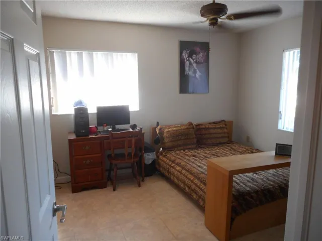 Bedroom with multiple windows, ceiling fan, a desk, a textured ceiling, and light tile patterned floors