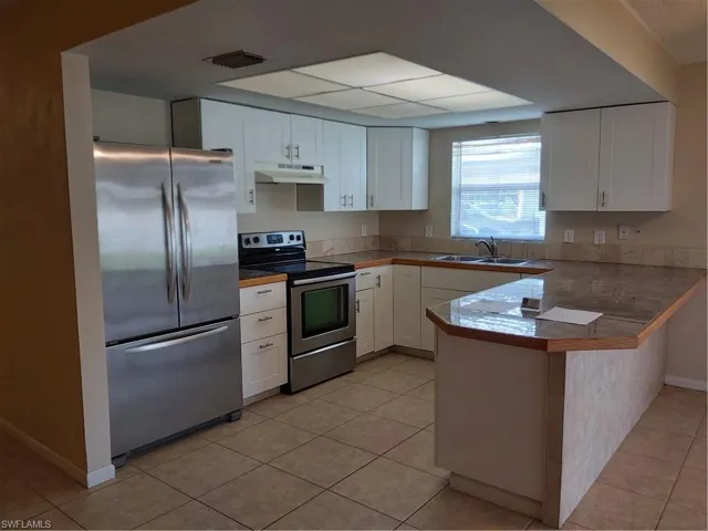 Kitchen with fridge, range, white cabinetry, light tile patterned floors, and a peninsula