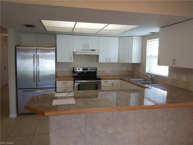 Kitchen featuring appliances with stainless steel finishes, white cabinets, under cabinet range hood, light tile patterned flooring, and a peninsula
