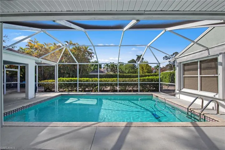 Screened outdoor pool area featuring a rectangular pool with tiled border, concrete surround, and steps with handrails