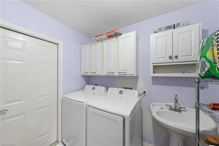 Dedicated laundry space featuring a pedestal sink with a chrome faucet, wall-mounted cabinetry, and a paneled door