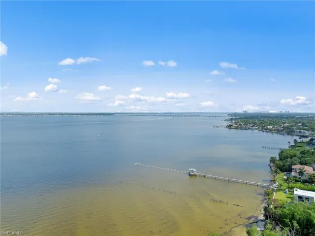 Expansive waterfront setting featuring a private dock with covered boat lift, surrounded by lush green landscaping
