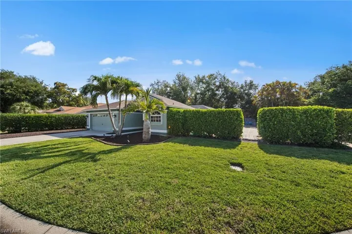 Single-story residence featuring a two-car garage, mature palm trees, and established perimeter hedges