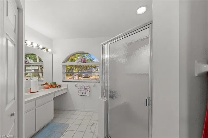 Bathroom featuring a glass-enclosed shower, white tile flooring, a dual-basin vanity with ample counter space, and arched windows